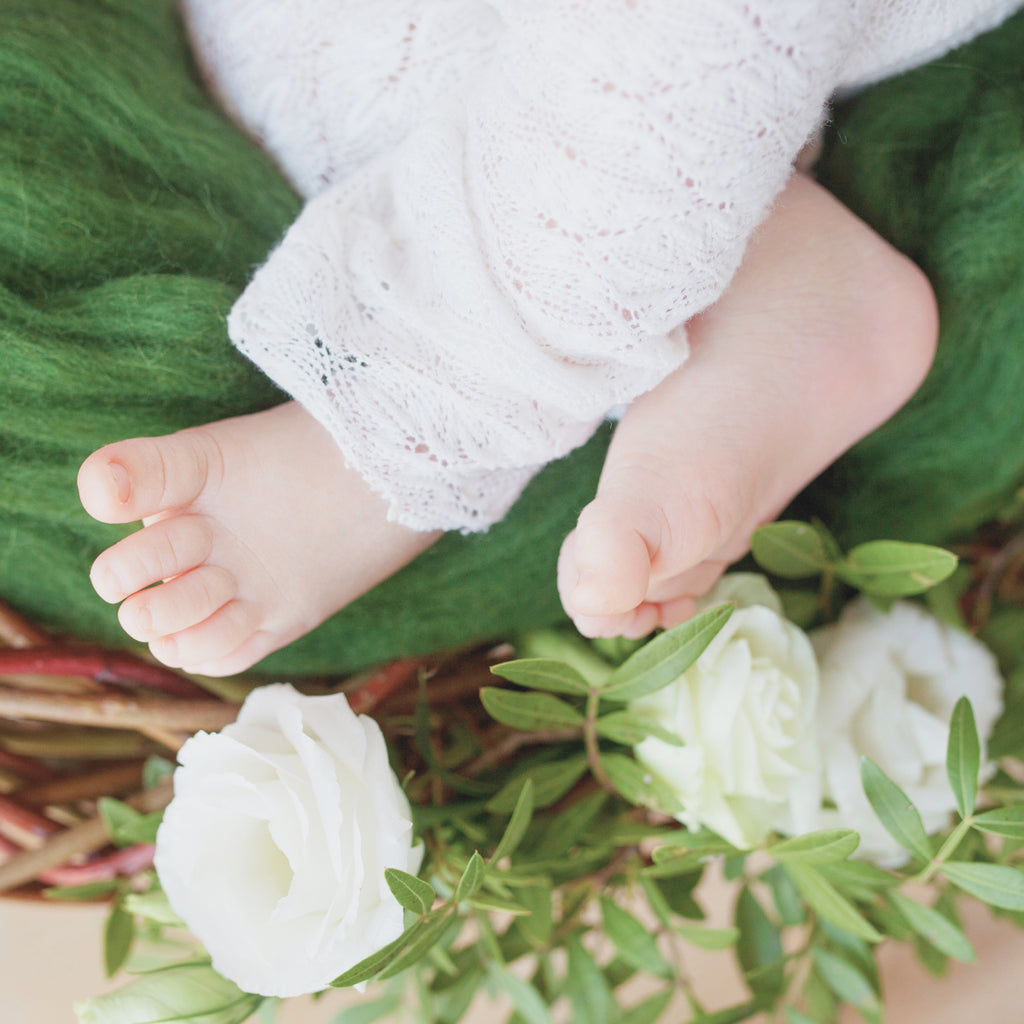 Green blanket, baby's feet and white roses.